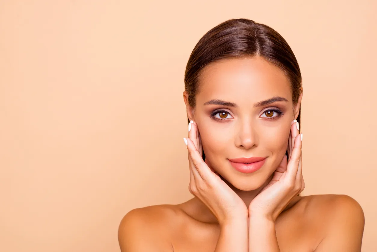 Smiling woman with flawless skin and hands on her face, representing non-surgical cosmetic treatments and aesthetic enhancement.