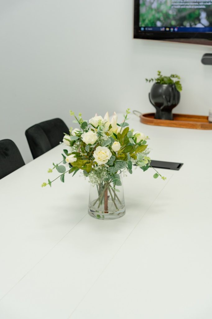 Floral arrangement on a white table in a group room, with a TV screen in the background, suitable for workshops and community programs.