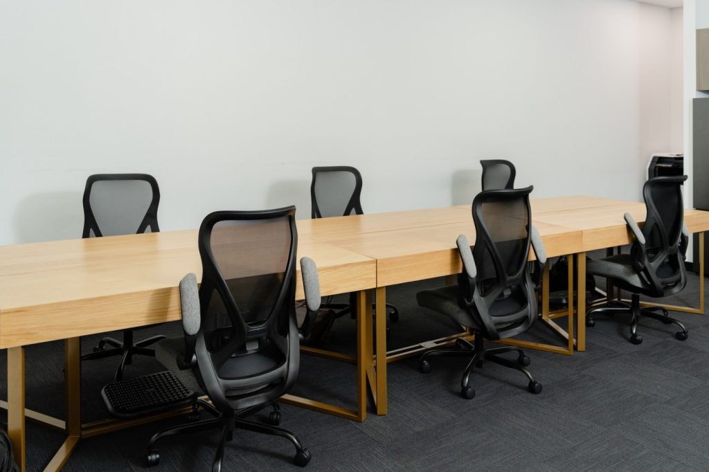 Hot desk workspace with wooden tables and ergonomic black chairs, designed for allied health professionals and flexible collaboration.