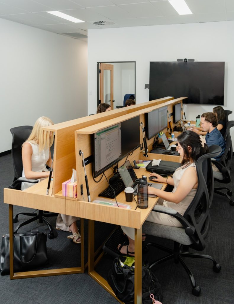 Hot desk workspace with allied health professionals collaborating, equipped with monitors and laptops, in a modern office setting.