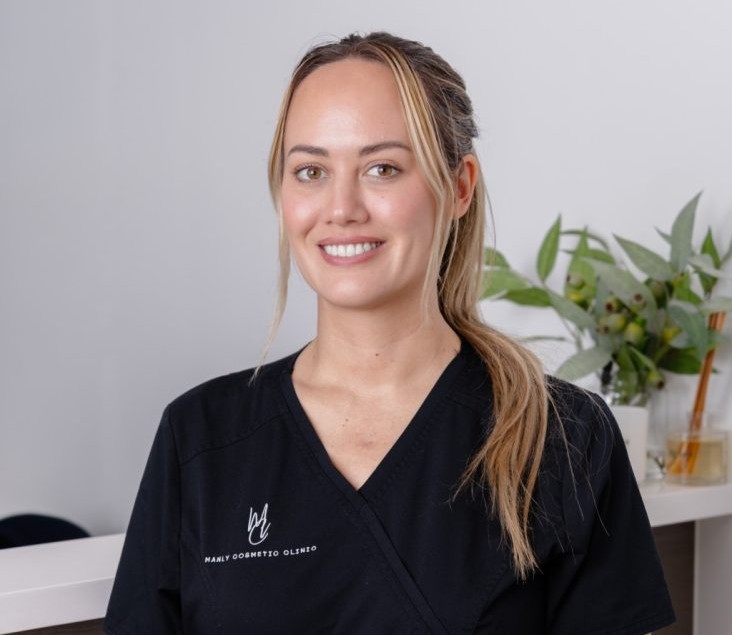 Smiling registered nurse in black scrubs, representing My Health Network, in a modern clinic setting with greenery in the background, emphasizing cosmetic aesthetics services.