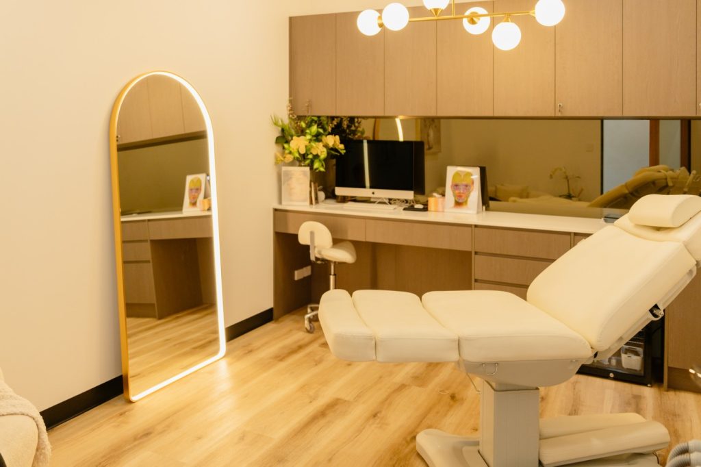 Premium medical room with electric treatment bed, mirror, desk area, and professional decor, emphasizing a clinical and private environment for healthcare practitioners.
