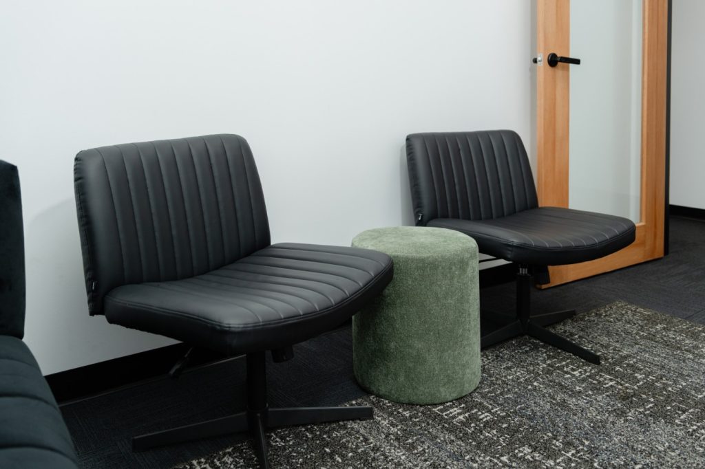 Black therapy chairs with a green ottoman in a soundproof consultation room, designed for privacy and comfort for health practitioners and clients.