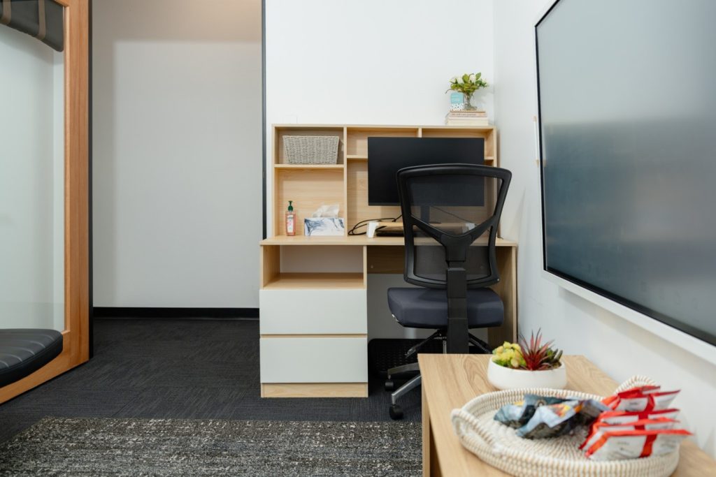 Private therapy room featuring a desk with a computer, ergonomic chair, and decorative plants, emphasizing a professional and welcoming environment for health practitioners.
