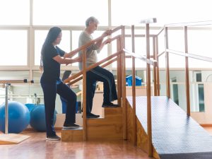 Physical therapist assisting patient with rehabilitation on stairs in a therapy facility, emphasizing support for emotional and physical well-being.